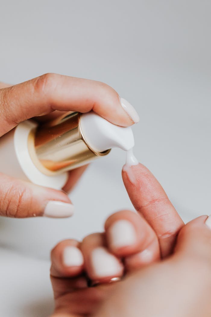 A woman applies skincare lotion from a pump bottle, showcasing manicured nails.